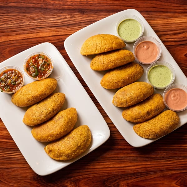 Two plates of golden empanadas with various dipping sauces on a wooden table.