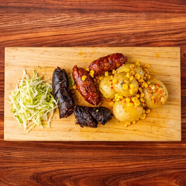 Sausages, blood sausage, potatoes with corn, and shredded cabbage on a wooden board.