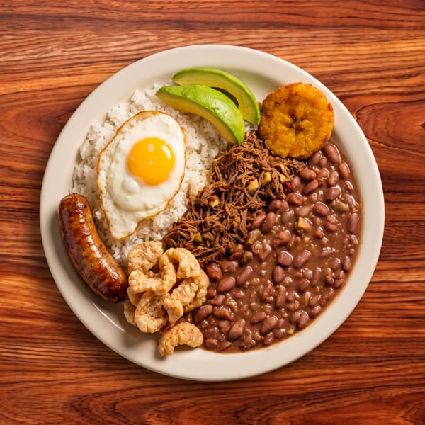 A white plate with rice, beans, shredded meat, fried egg, sausage, avocado, and plantain.