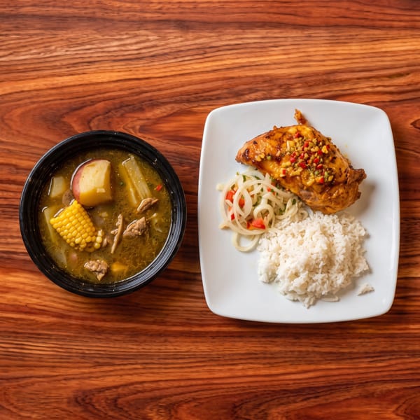 A bowl of soup with corn and potatoes next to a plate of chicken, rice, and onions.
